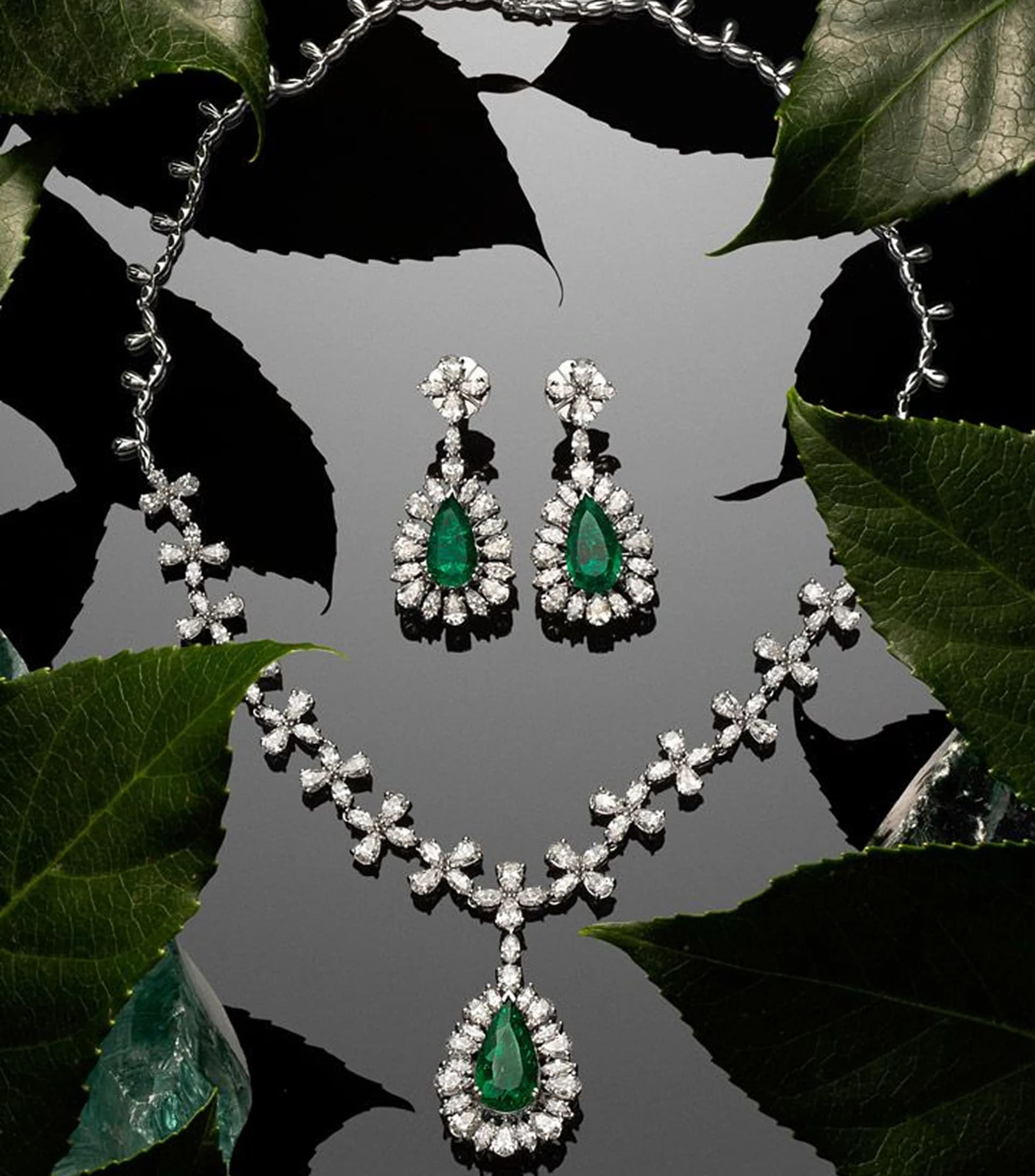 Elegant emerald and diamond jewelry set on dark leaves