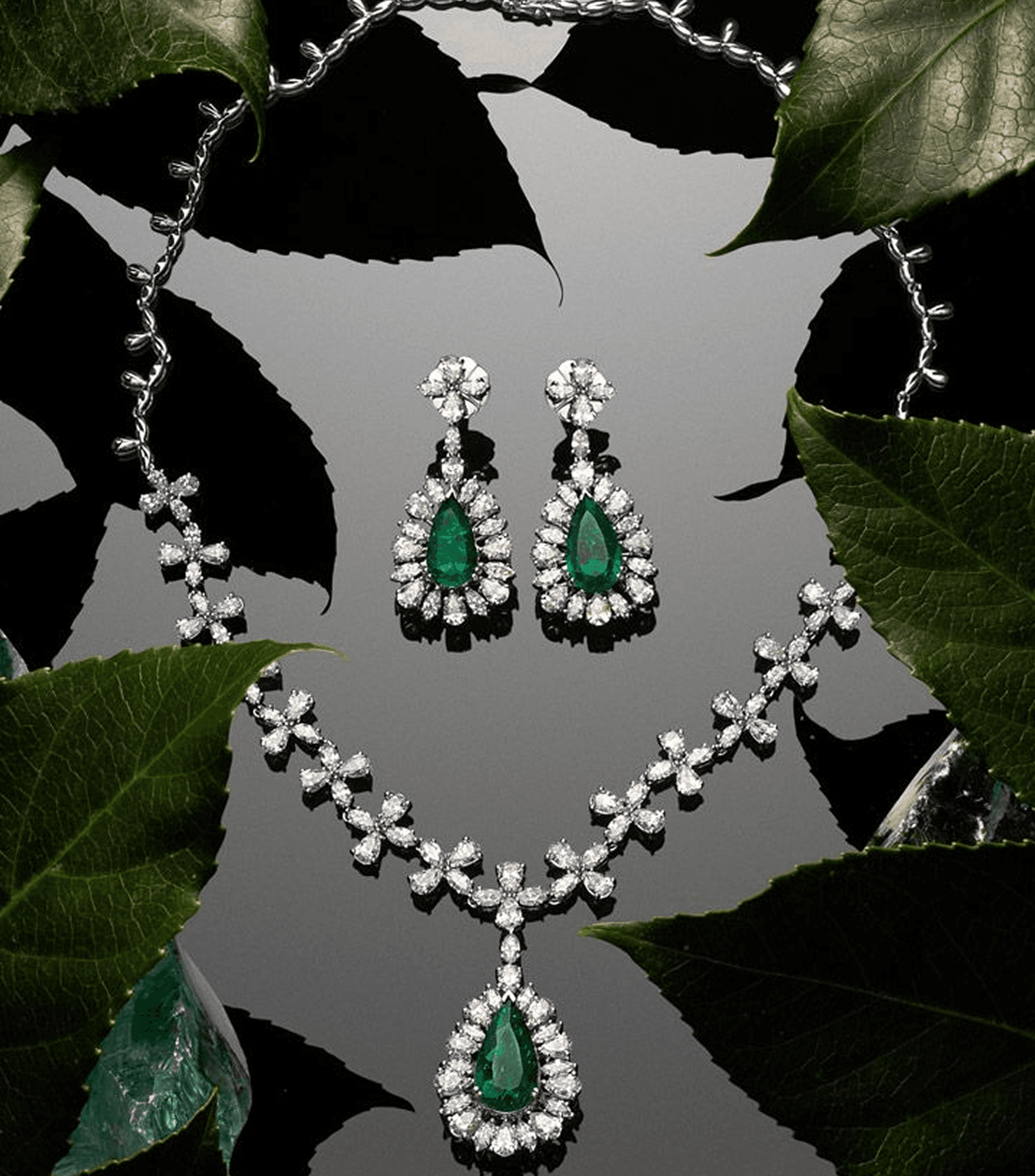 Elegant emerald and diamond jewelry set on dark leaves